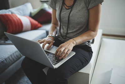 Midsection of industrial designer working on laptop in living room