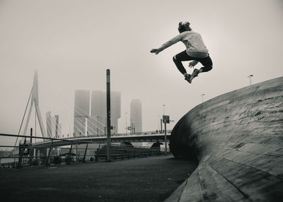 Rear view of man jumping on bridge against sky during foggy weather