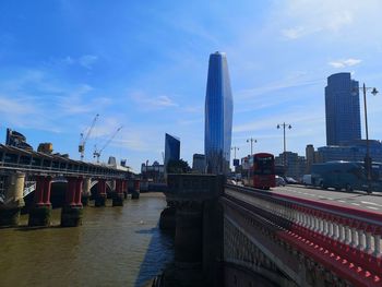 Bridge over river by buildings against sky in city