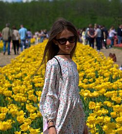 Young woman wearing sunglasses standing against yellow flowers