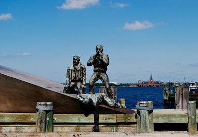 Statues by lake against sky