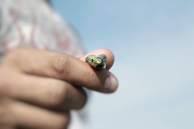 Close-up of human hand holding small snake against sky