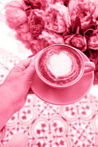 Woman holding cup of hot latte coffee with latte art. toned on viva magenta color of year 2023