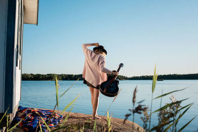 Woman walking on a rock at the beach holding her guitar in the sun