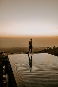 Full length of man standing by swimming pool during sunset