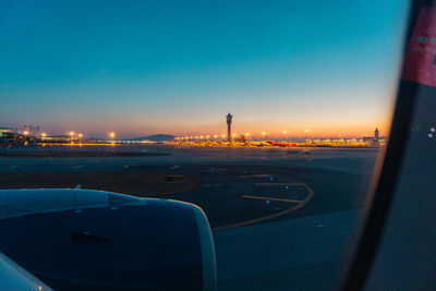 Airplane at airport runway against sky during sunset