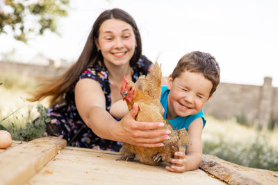 Happy mother having fun with her son and a chicken in countryside