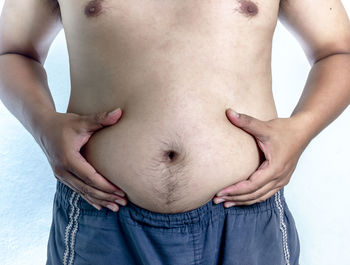 Midsection of shirtless man holding belly while standing against white background