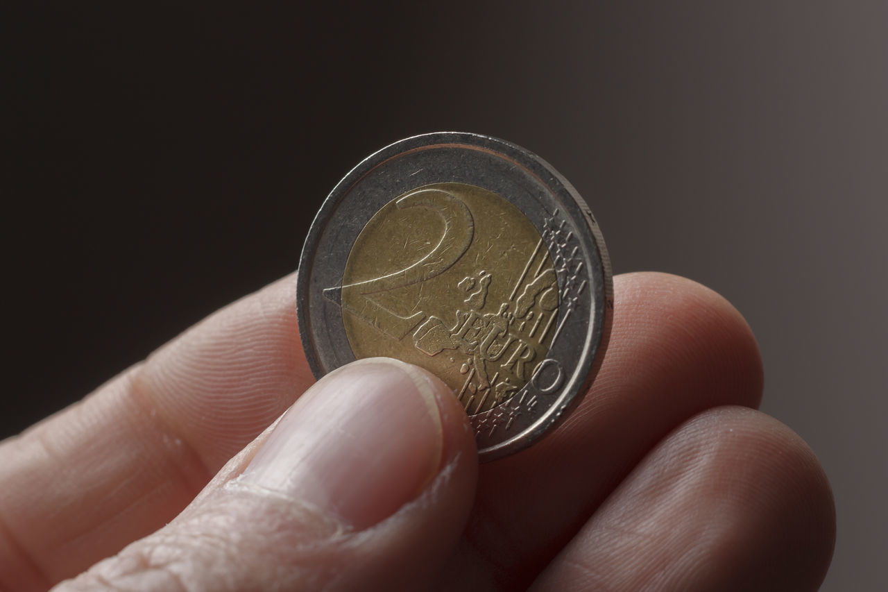 CLOSE-UP OF A HAND HOLDING COIN AGAINST BLACK BACKGROUND