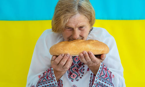 Senior woman smelling bread against against ukrainian flag