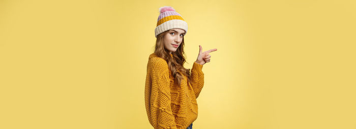 Portrait of young woman standing against yellow background