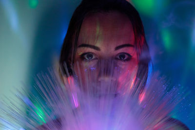 Close-up portrait of young woman holding illuminated fiber optic against wall