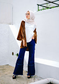 Full length portrait of young woman standing against wall