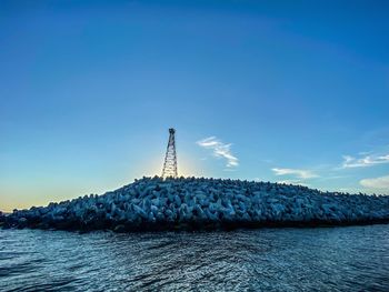 Lighthouse by sea against blue sky