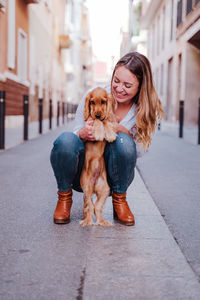 Smiling woman playing with dog in city