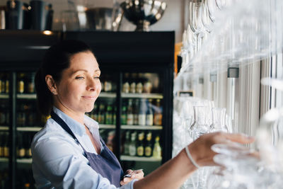 Smiling woman arranging wineglasses in restaurant