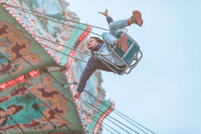 Low angle view of girl playing on chain swing ride against clear sky