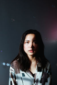 Portrait of young woman standing against illuminated wall