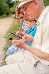 Grandson teaching digital tablet to grandmother while grandfather using mobile phone in public park