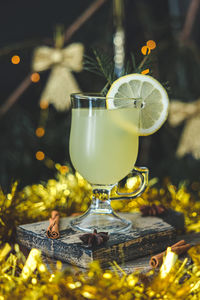 A glass of lemon drink with a circle of lemon and cinnamon sticks on a cutting board 