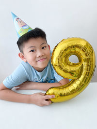 Portrait of smiling boy holding yellow against white background