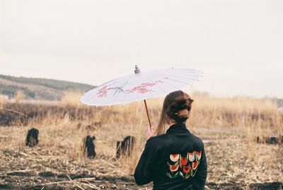 Rear view of woman standing with umbrella on field against sky