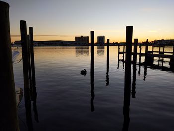 Wooden posts in lake against sky during sunset