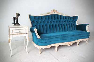 Antique phone on table by vintage sofa against wall at home