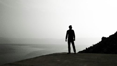 Rear view of a silhouette man overlooking calm sea