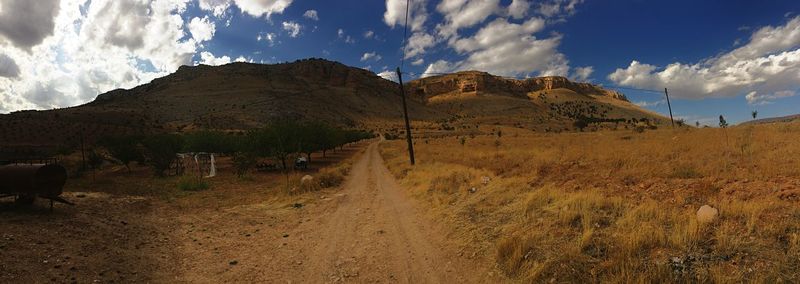 Panoramic view of dirt road amidst field against sky