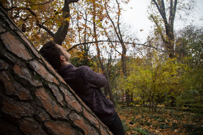 Portrait of man sitting on tree trunk in forest