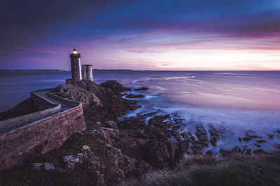 Lighthouse by sea against sky during sunset