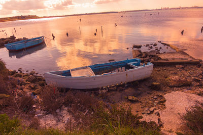 Boat moored on beach against sky during sunset