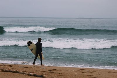 Rear view of surfer standing on shore