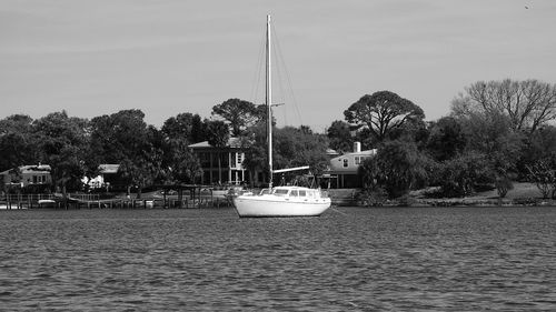 Boats sailing in river by trees against sky