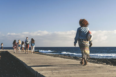 Rear view of woman walking on pier over sea against sky