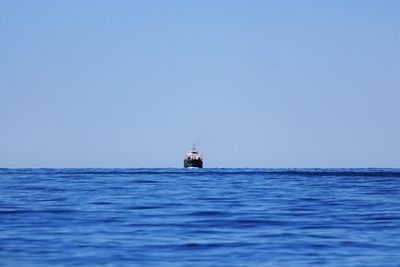 Boat sailing on sea against clear blue sky