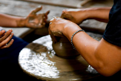 Cropped hands of people working on pottery wheel