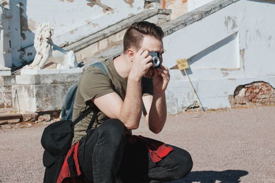 Young man photographing while crouching on road