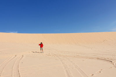 Man on sand dune in desert against clear blue sky