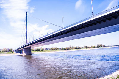 Suspension bridge over river against sky in city