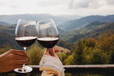 Man and woman clinking with glasses of red wine with a beautiful scenic mountain view. 