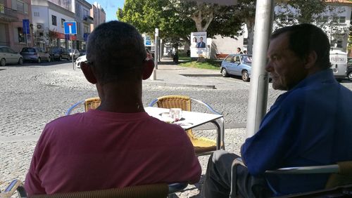 Rear view of men sitting at sidewalk cafe in city