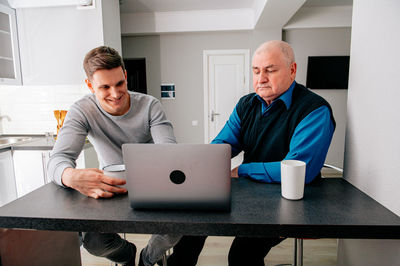 Happy young man with grandfather using laptop at table
