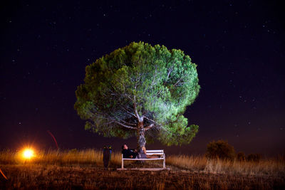 Young man resting on bench by tree against star field at night