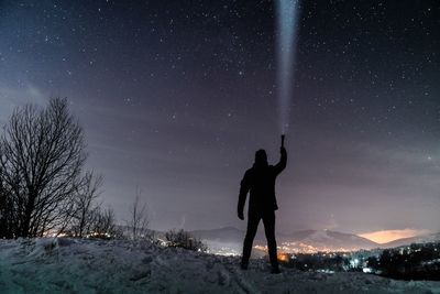 Full length of silhouette man holding illuminated flashlight while standing against star field at night