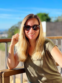 Portrait of young woman wearing sunglasses while sitting at beach