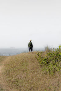 Rear view of woman walking on field against clear sky