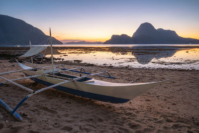 Boat at beach against clear sky during sunset