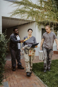 Female construction manager discussing with workers while walking outside house